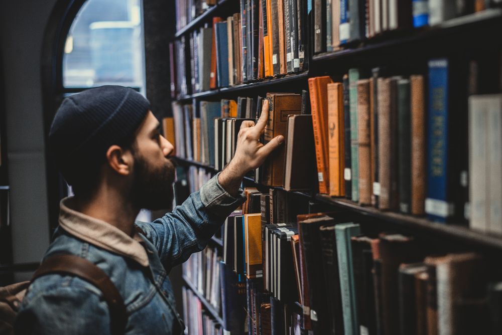 Photo of a man in a library picking up a book.